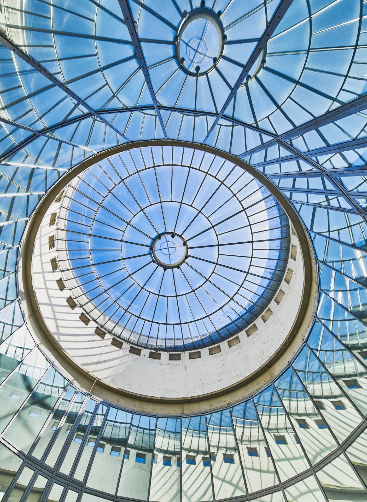 Blick durch ein rundes, glasüberdachtes Lichtdesign mit geometrischen Mustern und strahlend blauem Himmel.