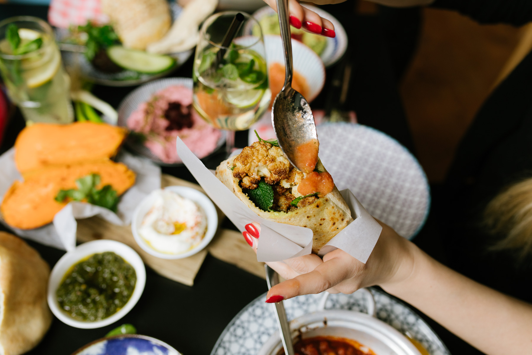 Eine Hand hält einen Wrap, umgeben von köstlichen Gerichten und Getränken auf einem Tisch.
