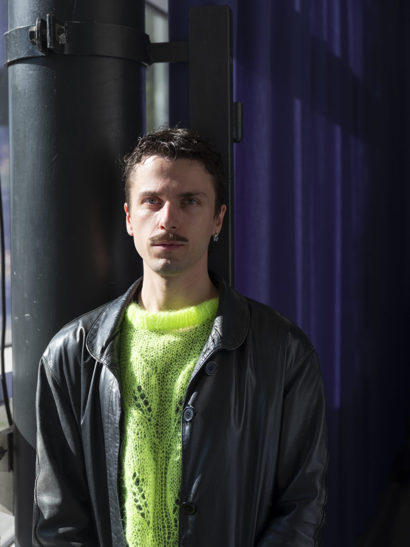 Zu sehen ist Philipp Lange. Er trägt einen neongelben Pullover und darüber eine schwarze Lederjacke.